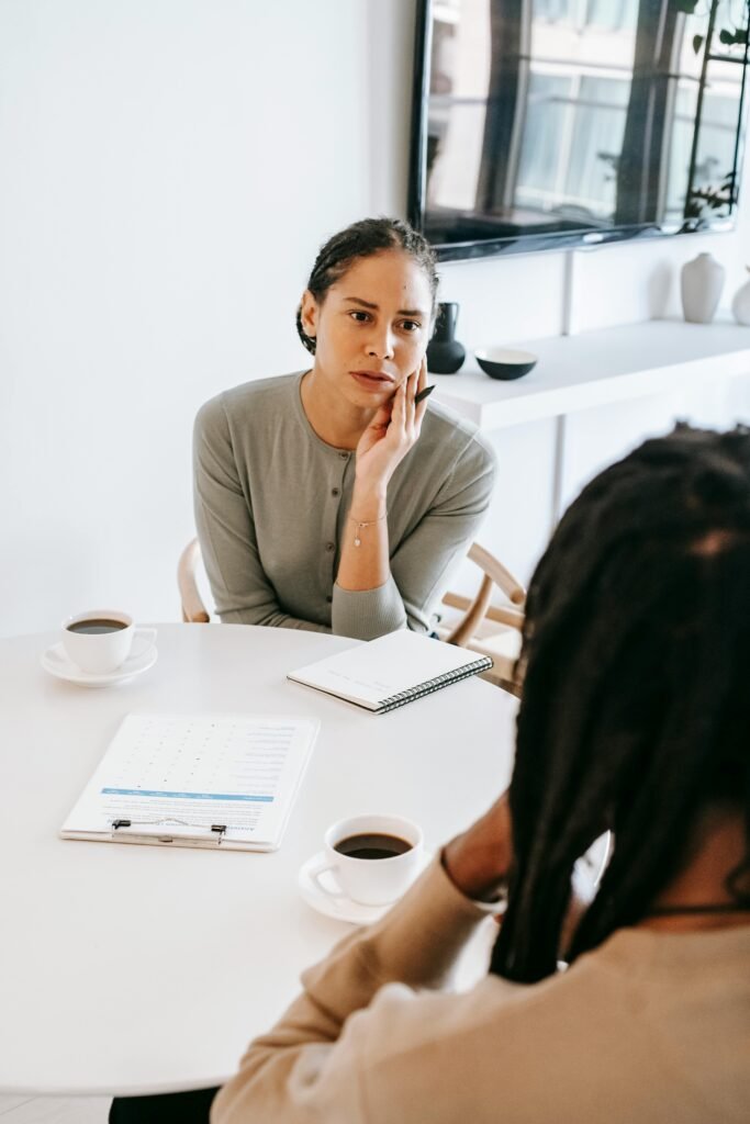 Serious ethnic female consultant listening to black male client problems while sitting at round table together in light psychology center